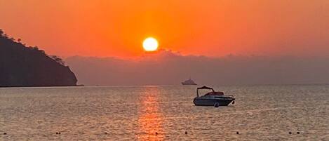 A sunset over a calm sea with a boat and a distant ship.