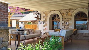 Un espacio de estar al aire libre acogedor con pared de piedra, mobiliario de madera y una pérgola cubierta de enredaderas con flores.