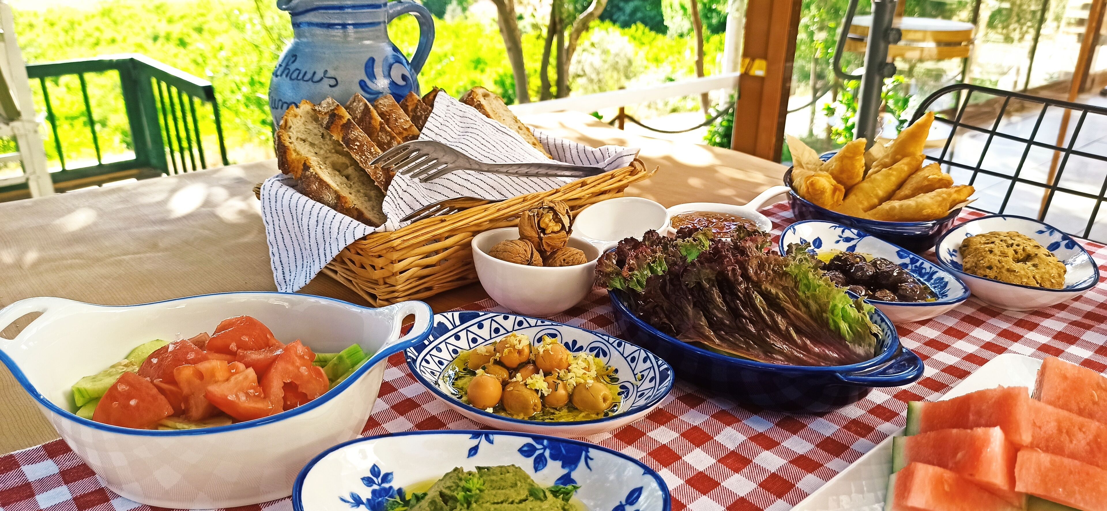A table set with various dishes including bread, salad, and dips, outdoors with a checkered tablecloth.