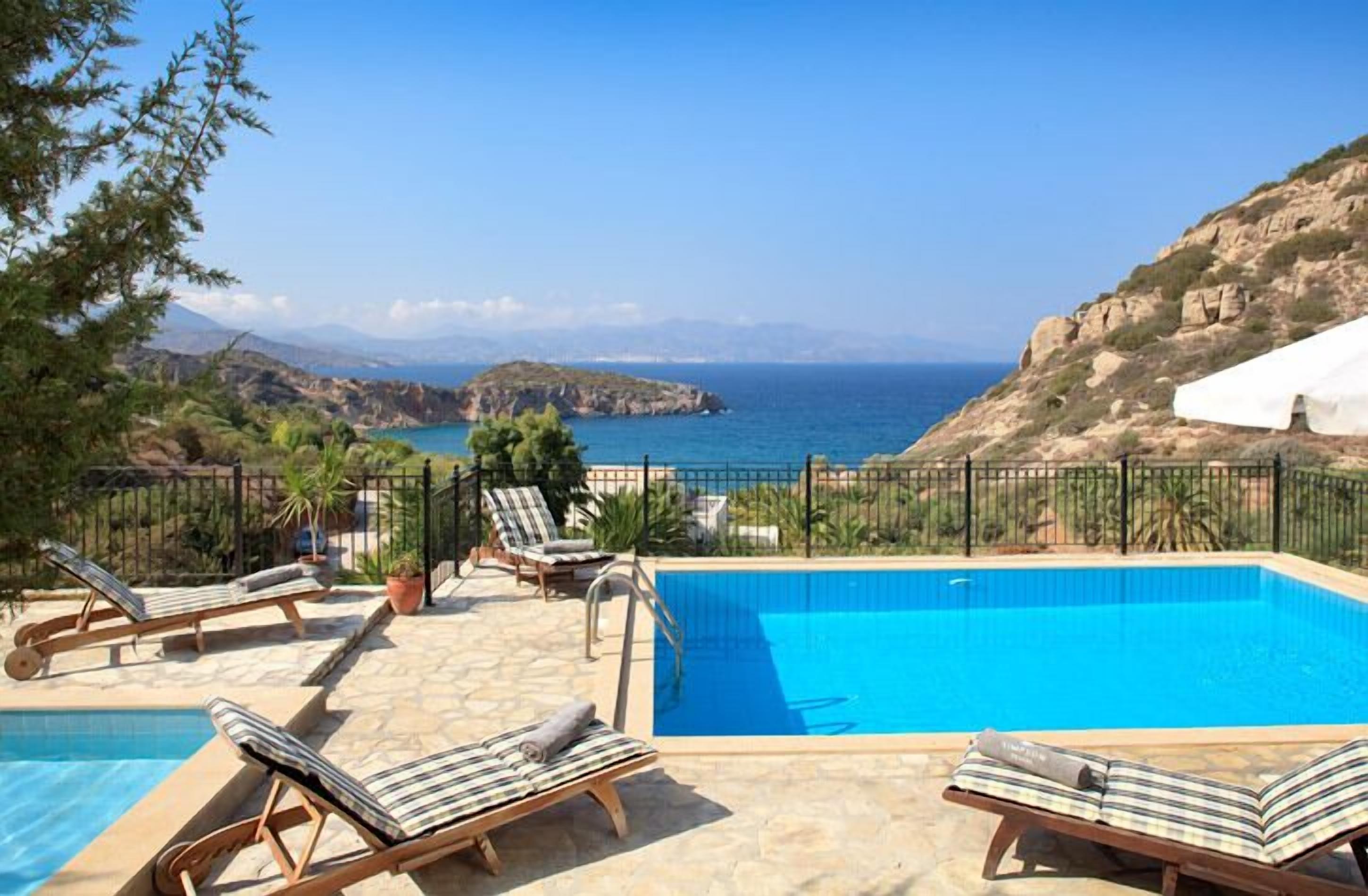 Area piscina con lettini, vista libera sul mare e montagne sullo sfondo.