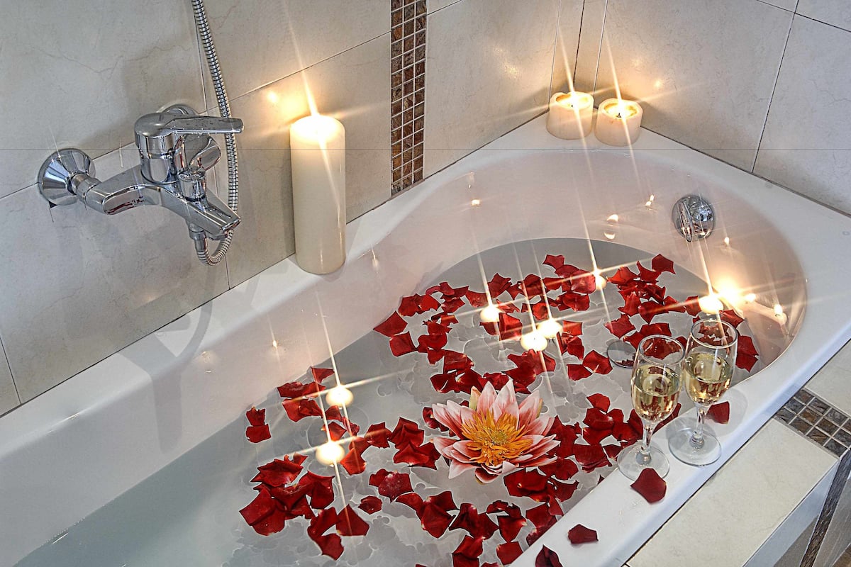 Una bañera con pétalos de rosa, velas y dos copas de vino.