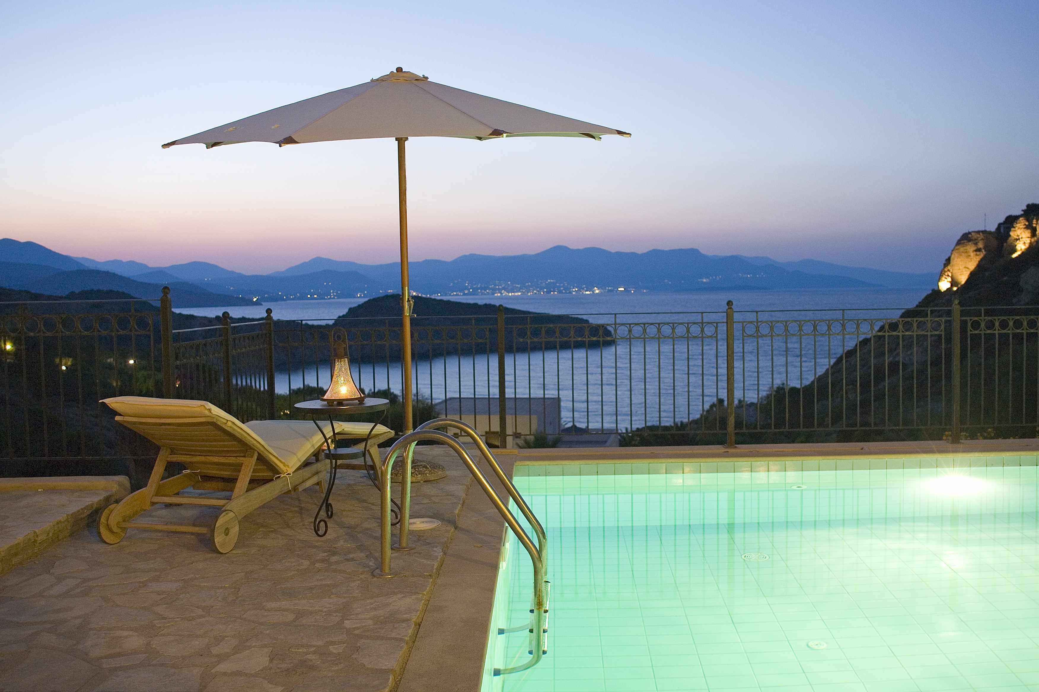 Una piscina con vistas al mar y a las montañas, una tumbona y una sombrilla.