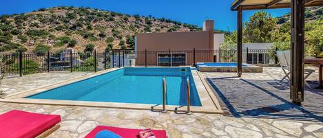 A swimming pool with stone flooring, red lounge chairs, and a wooden pergola structure.