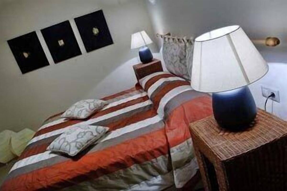 Una cama con ropa de cama a rayas, dos lámparas de noche y un enchufe en la pared.