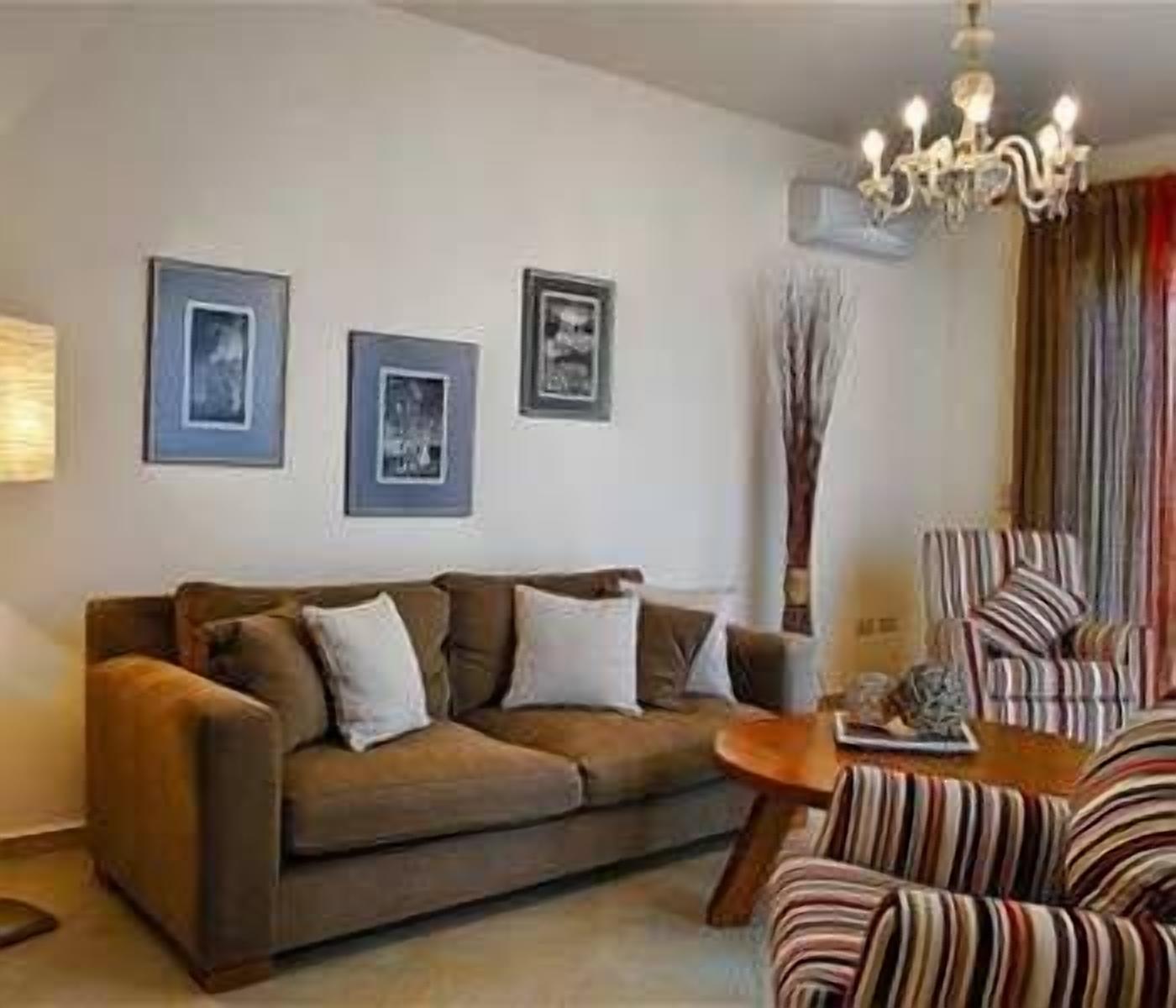 A living room with a brown sofa, two framed pictures on the wall, a striped armchair, and a chandelier.