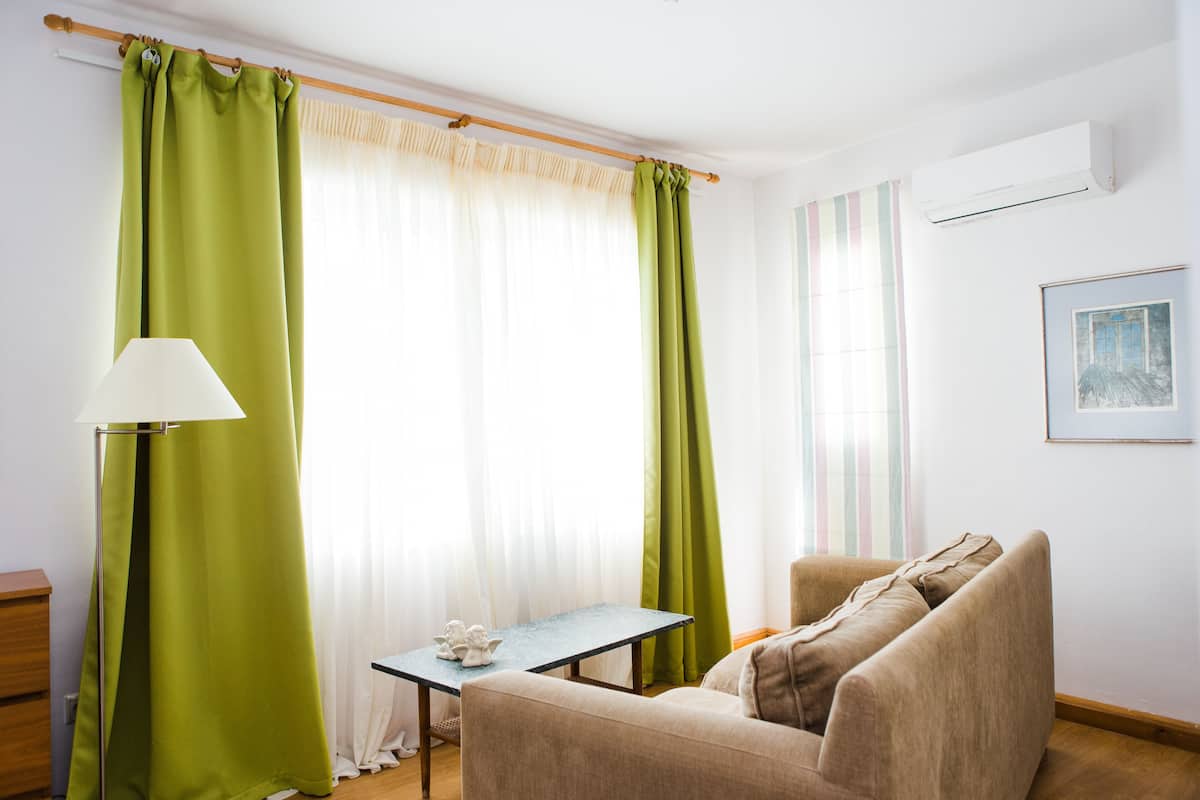 Una habitación con sofá, una mesita, una lámpara y una ventana con cortinas verdes.
