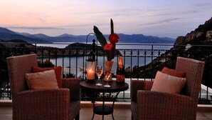 Un ensemble de meubles de balcon en osier, composé d’une chaise et d’une table, agrémenté d’une bouteille, de verres et d’une bougie, et offrant une vue sur un plan d’eau et des montagnes.