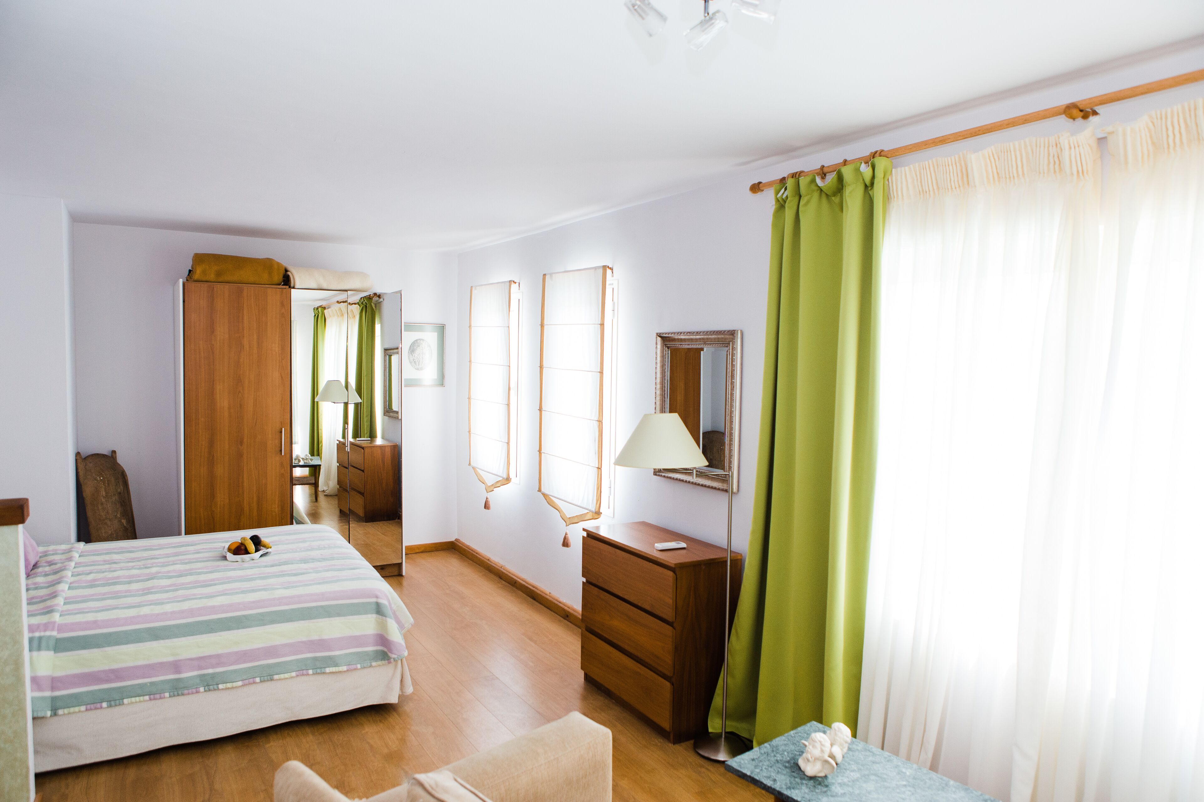 A bedroom with a bed, a dresser, a mirror, and a window with curtains.