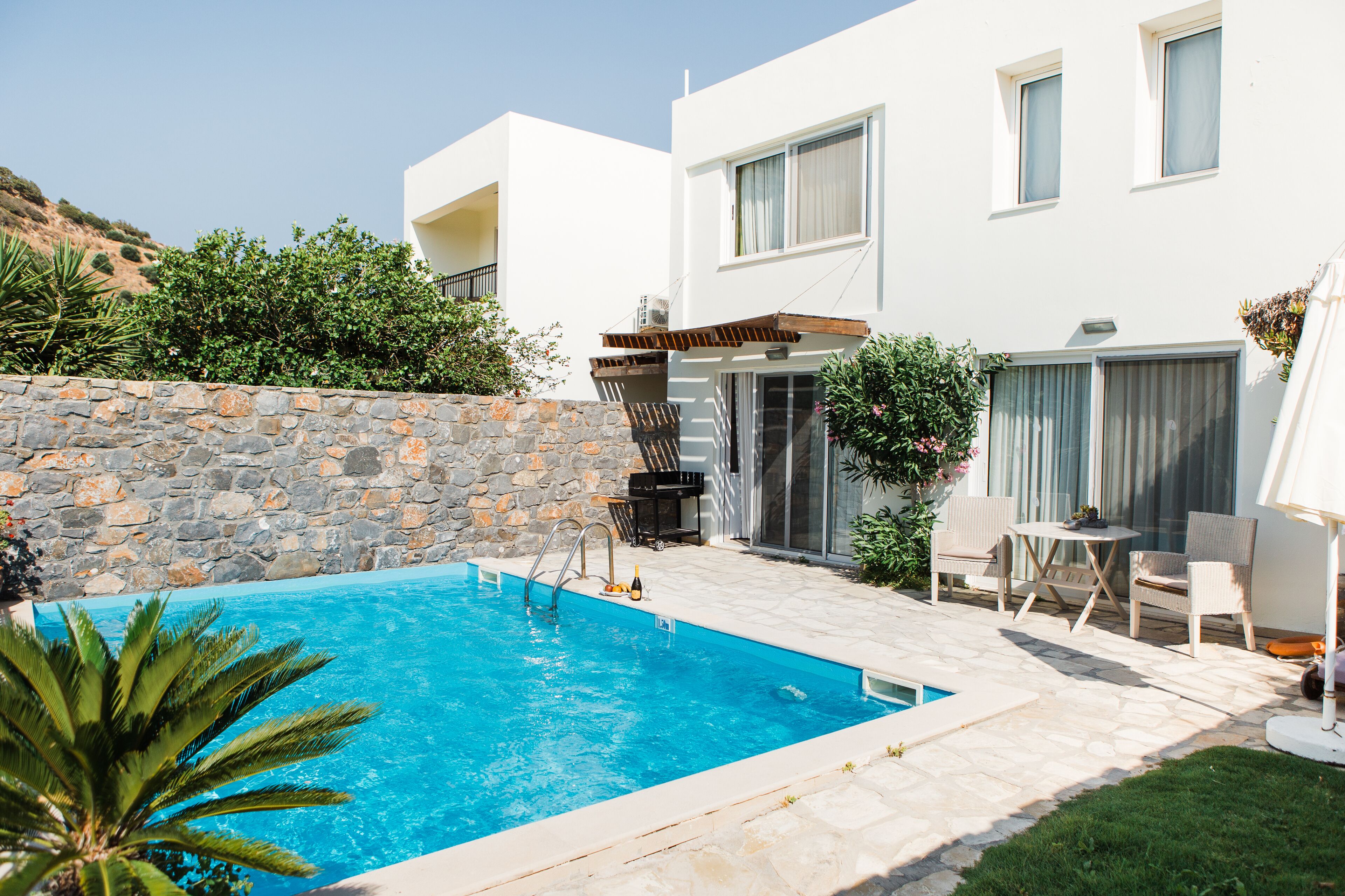 A modern house with a swimming pool, stone wall, and outdoor furniture.