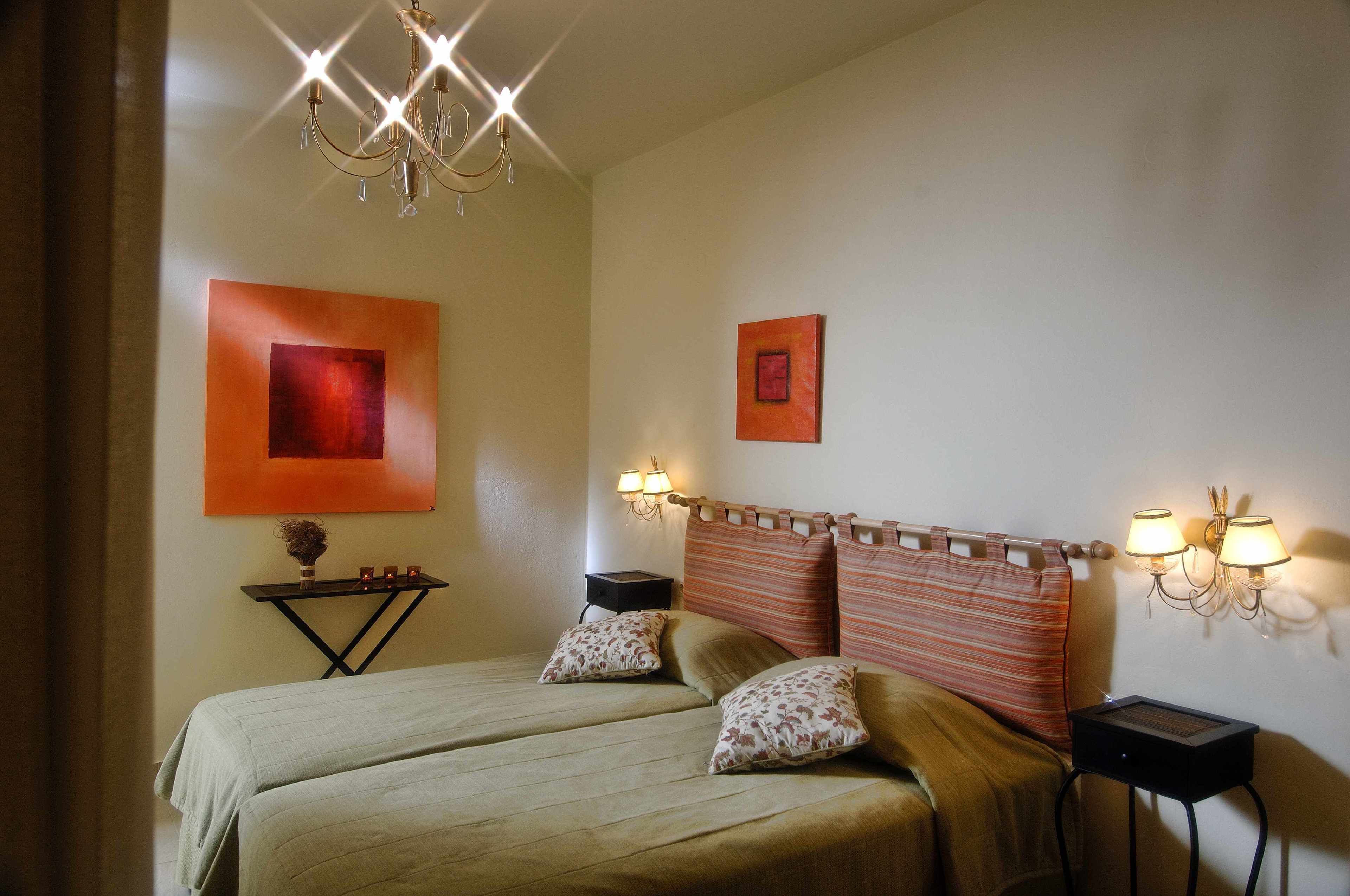 A double bed with two pillows, a nightstand with a lamp, and a wall-mounted light fixture.