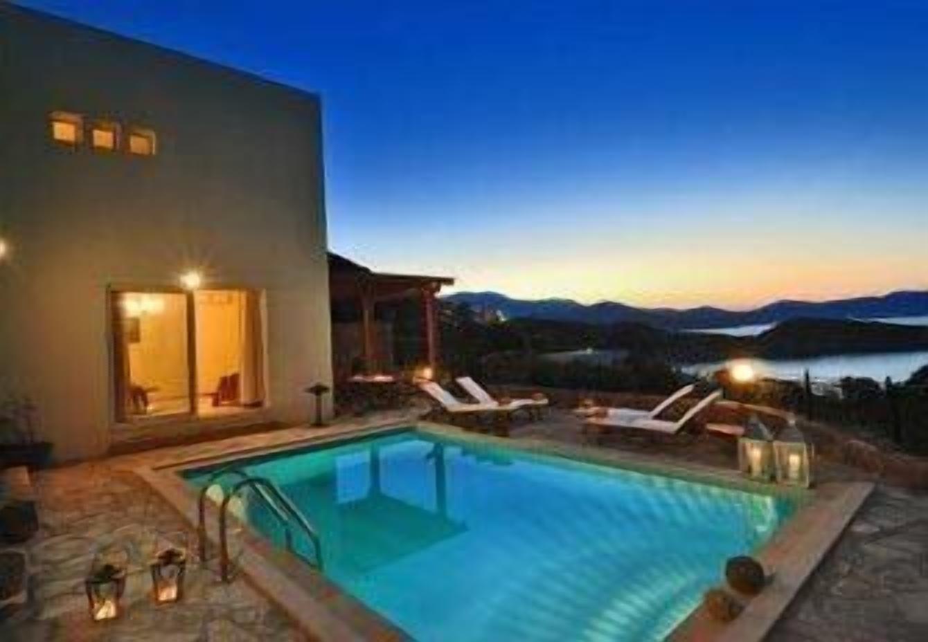 A swimming pool with lounge chairs and a view of the mountains at dusk.