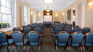 Un salón de conferencias con filas de sillas azules, una mesa grande y una araña.