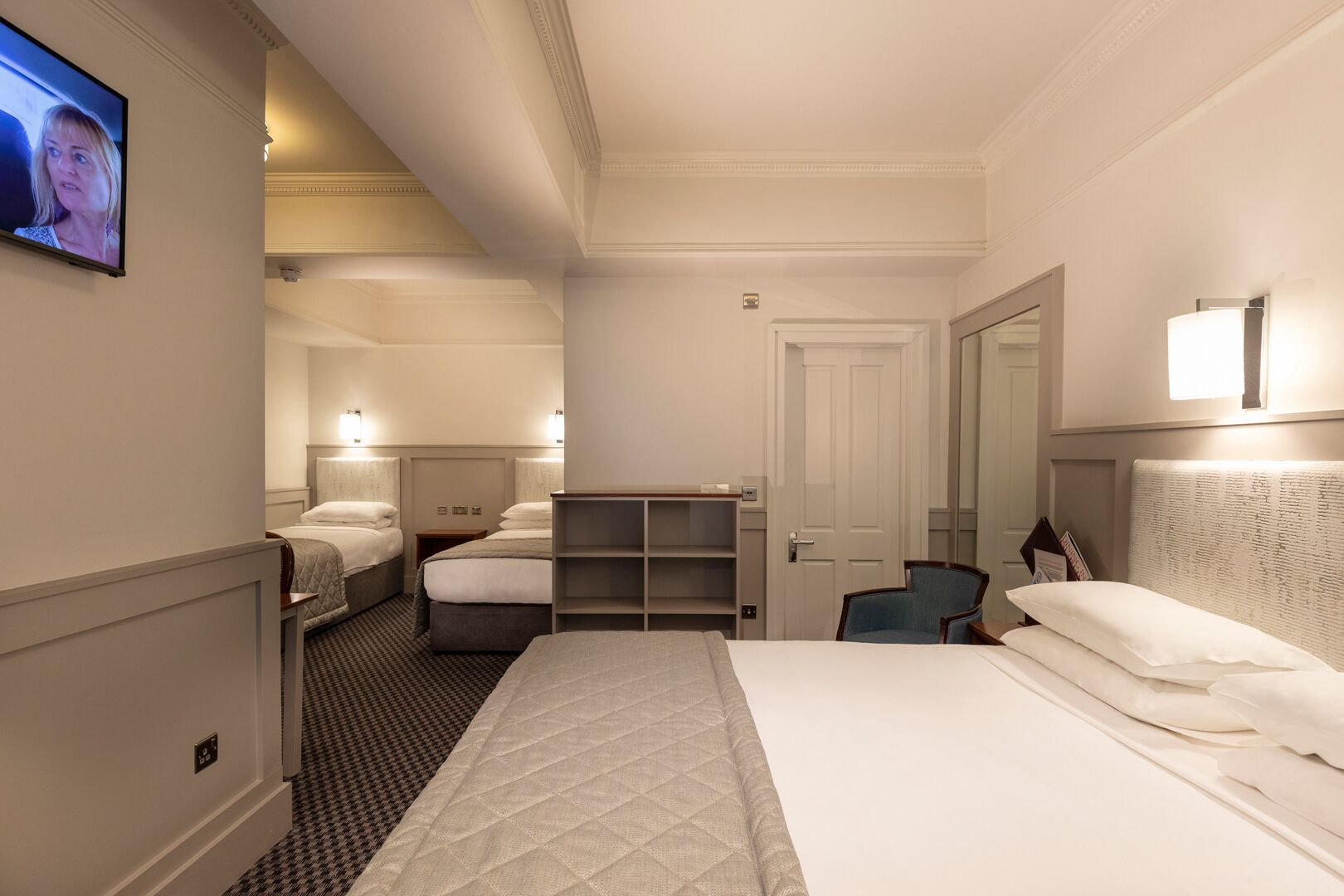 A hotel room with two beds, a television, a desk, and a chair.
