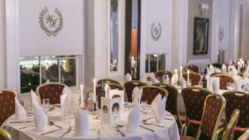 Un comedor elegante con mesas redondas, sillas tapizadas en rojo y manteles blancos.