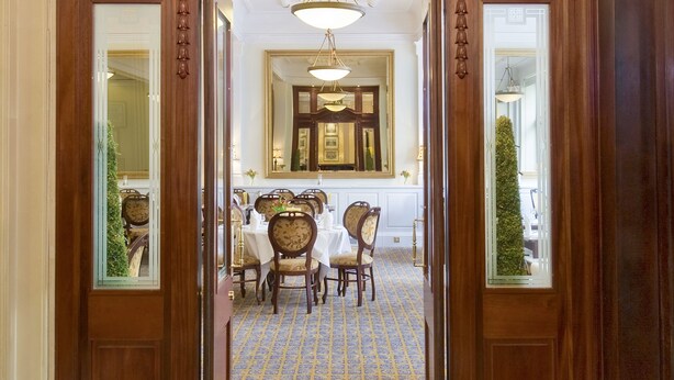 Una entrada imponente con candelabro, puertas de madera y un comedor con sillas y una mesa.