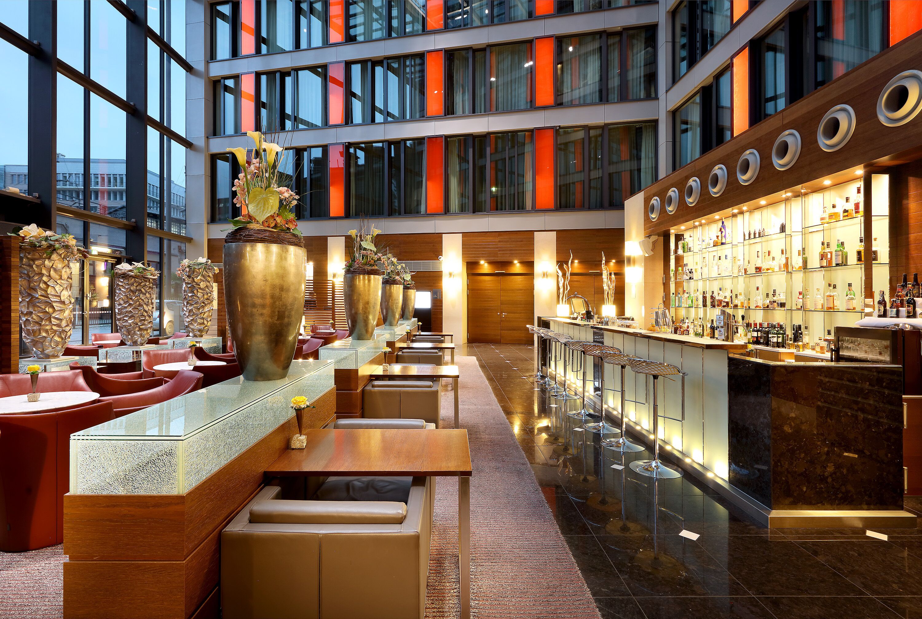 A modern hotel lobby with a long bar, seating area, and large windows.