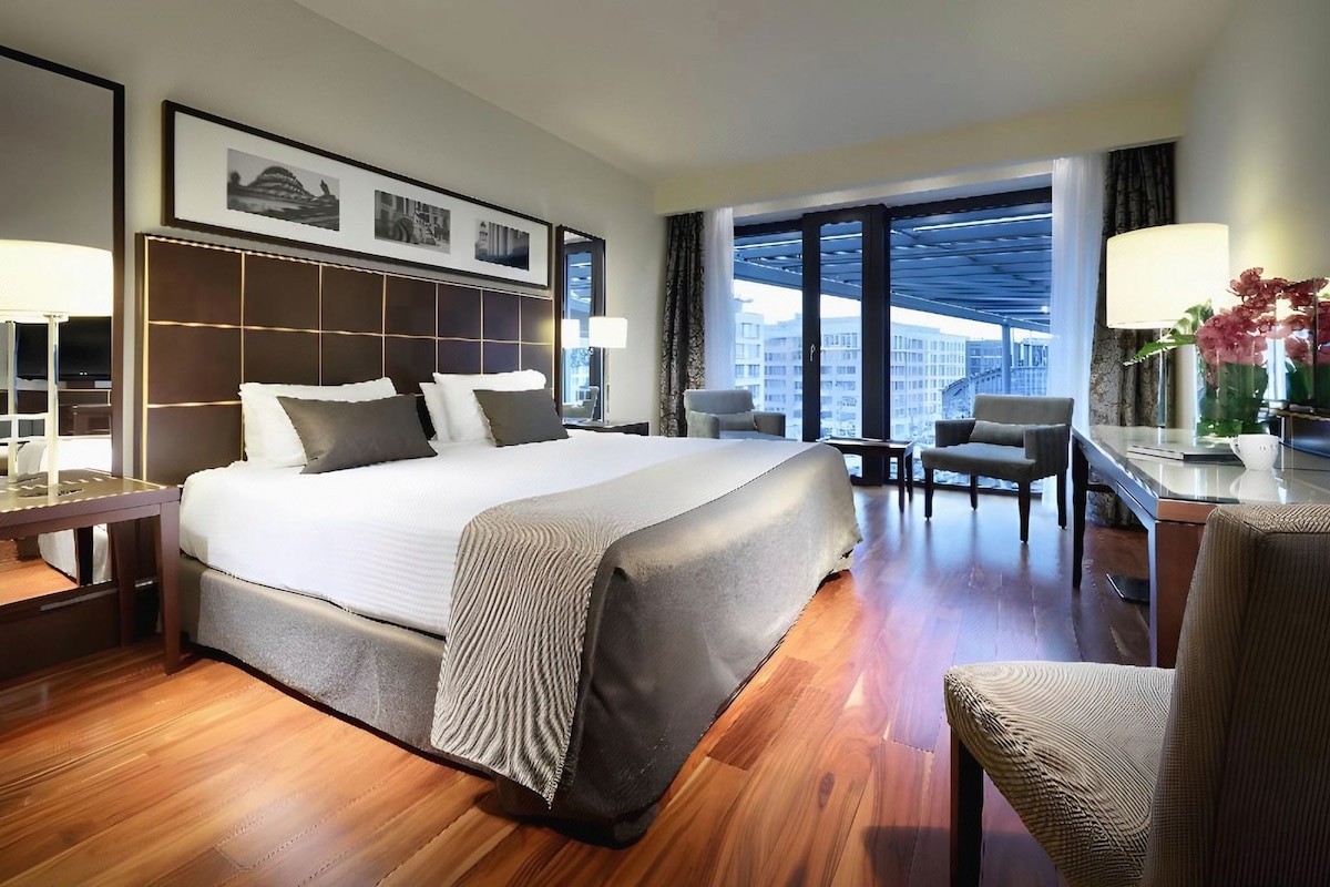 Habitación de hotel con una cama grande, un escritorio, una silla y vistas a la ciudad.