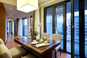 Habitación de hotel con zona de comedor, cama y ventana grande con vista a la ciudad.