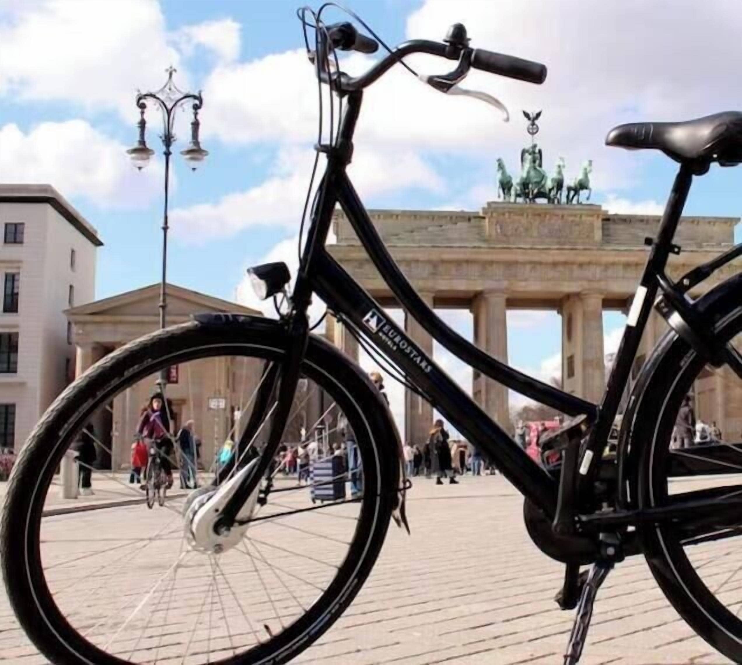 Uma bicicleta preta com a marca 'LE ROYALE', estacionada em frente a um edifício histórico de arquitetura clássica.