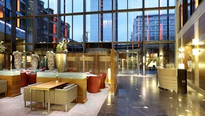 Un hall d’hôtel moderne avec une façade en verre, des espaces de détente et un comptoir d’accueil.