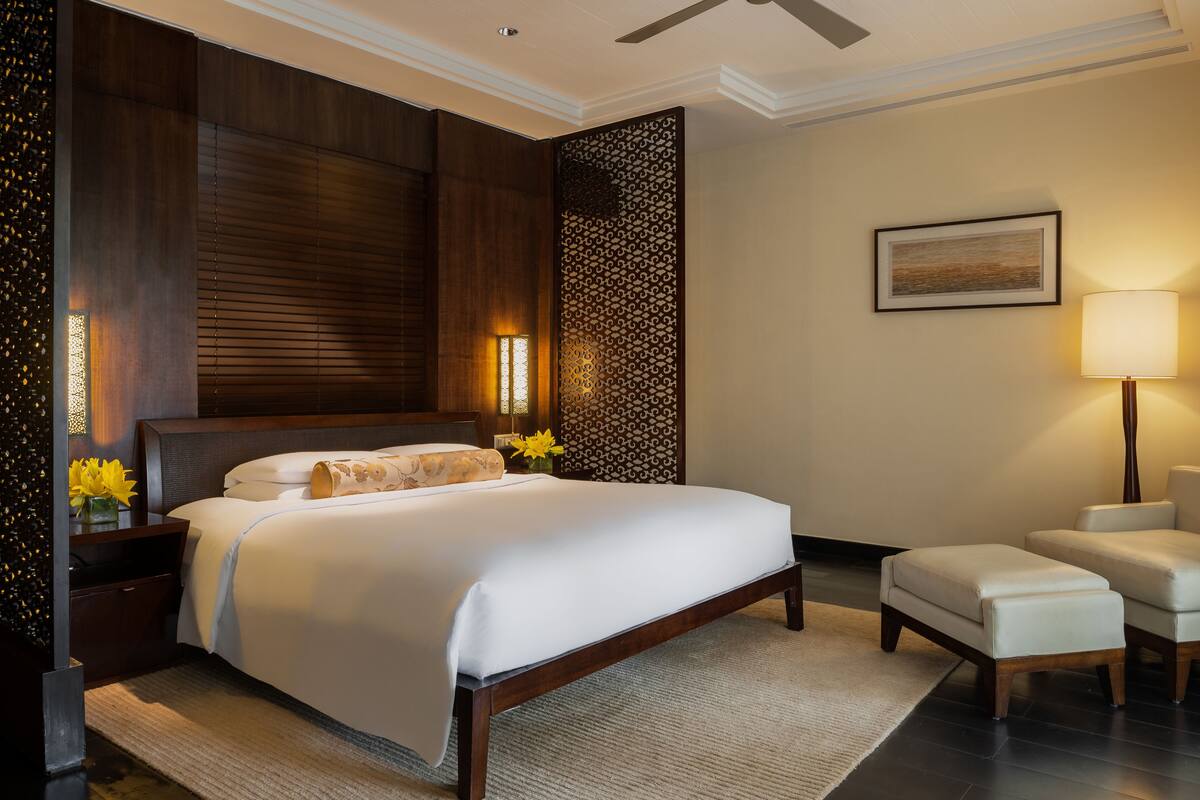 Habitación de hotel con una cama grande, una mesita de noche con lámpara, una silla y un panel decorativo en la pared.