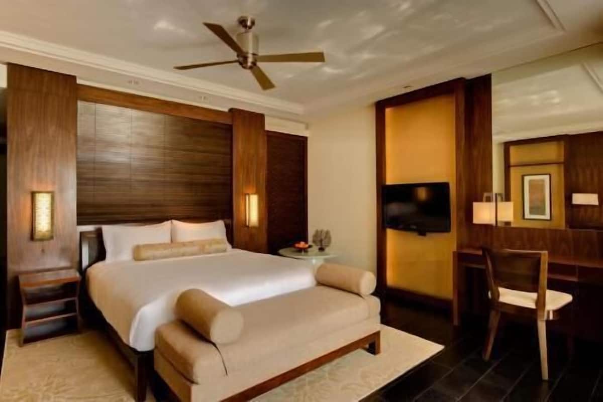 Habitación de hotel con una cama grande, un escritorio, una silla, un ventilador de techo y un televisor de pantalla plana.