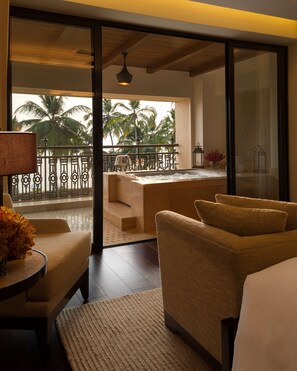 A hotel room with a balcony, a sofa, a table with a lamp, and a view of palm trees. - Grand Hyatt Goa (Panaji)