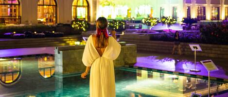 A woman in a white dress standing by a pool with a building in the background.