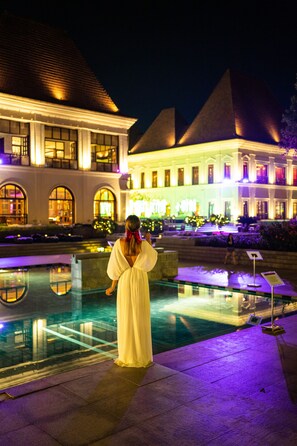 A woman in a white dress standing by a pool with a building in the background. - Grand Hyatt Goa (Panaji)