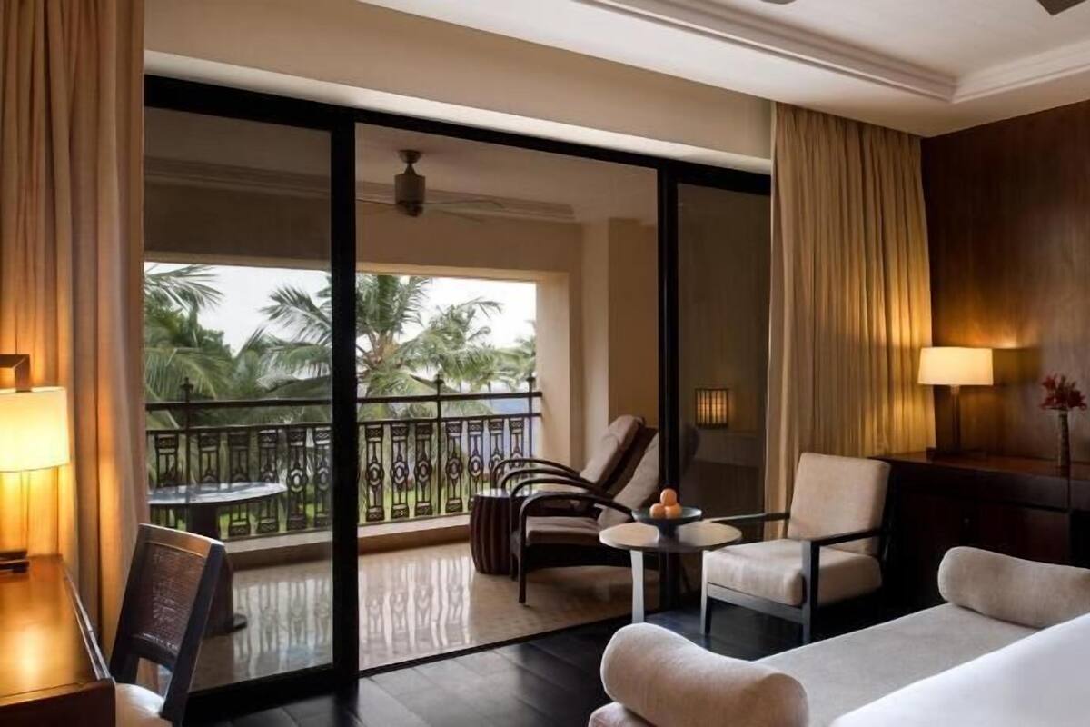 Habitación de hotel con balcón, dos sillones, una mesita y una cama.