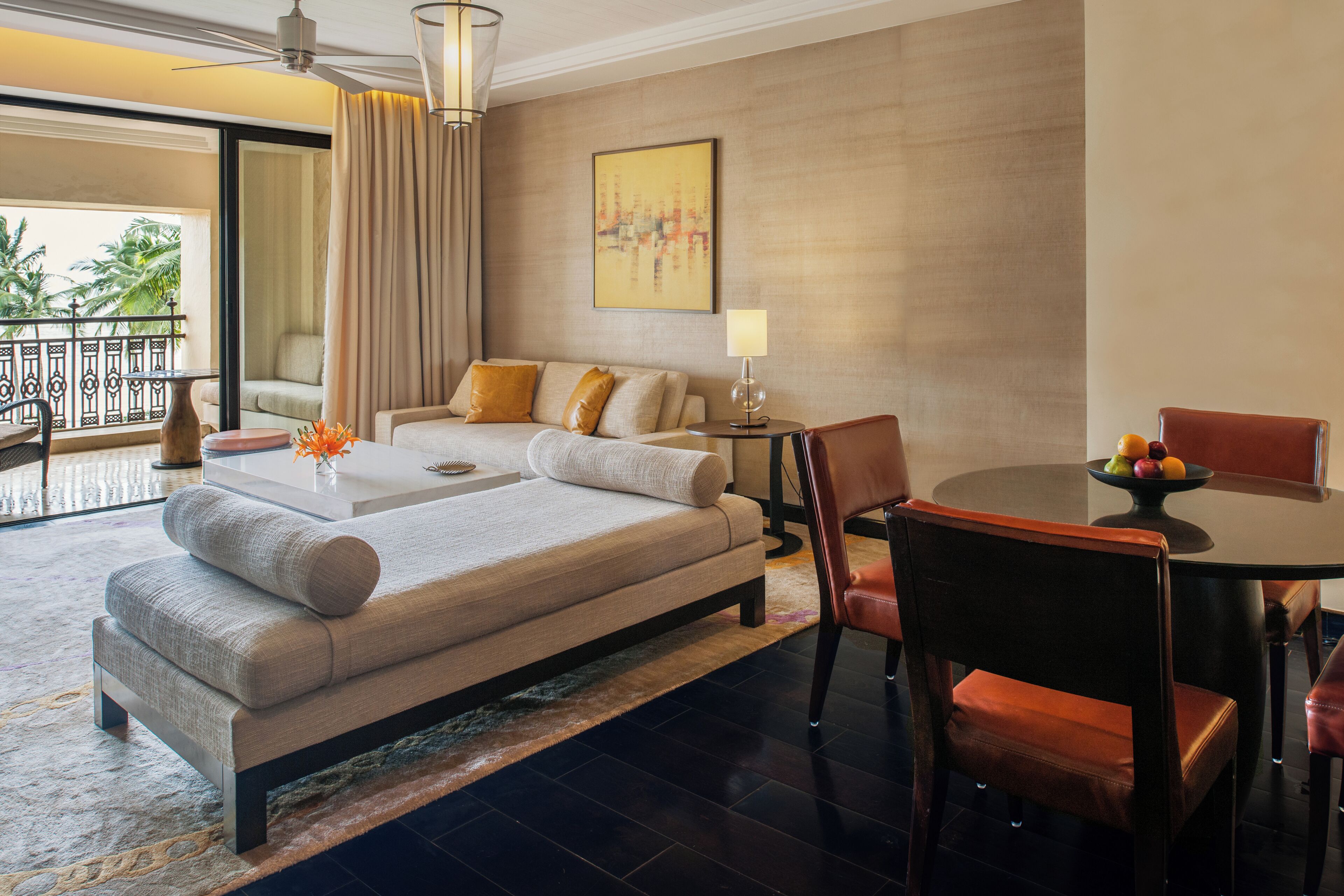 Habitación de hotel moderna con una cama grande, una mesa de comedor con sillas, un balcón con vistas a palmeras y un cuadro en la pared.