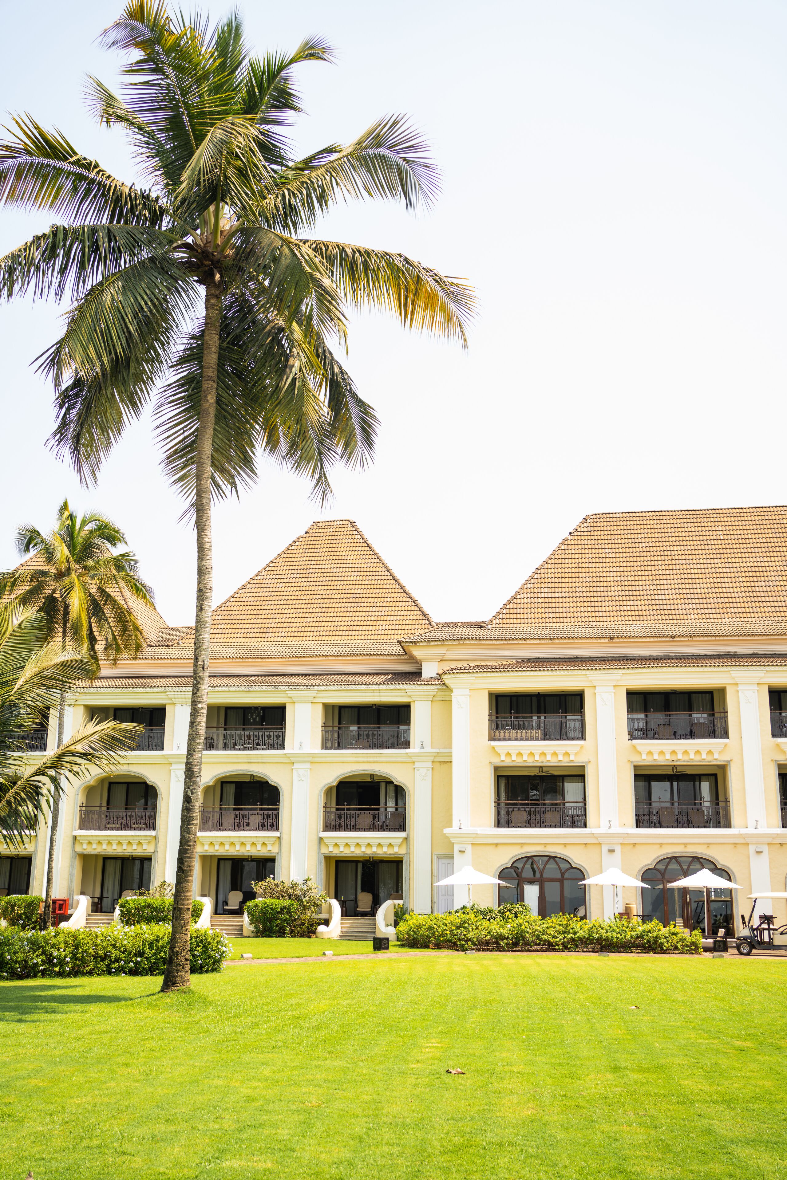 A large building with a symmetrical facade, multiple balconies, and a well-maintained lawn with palm trees.