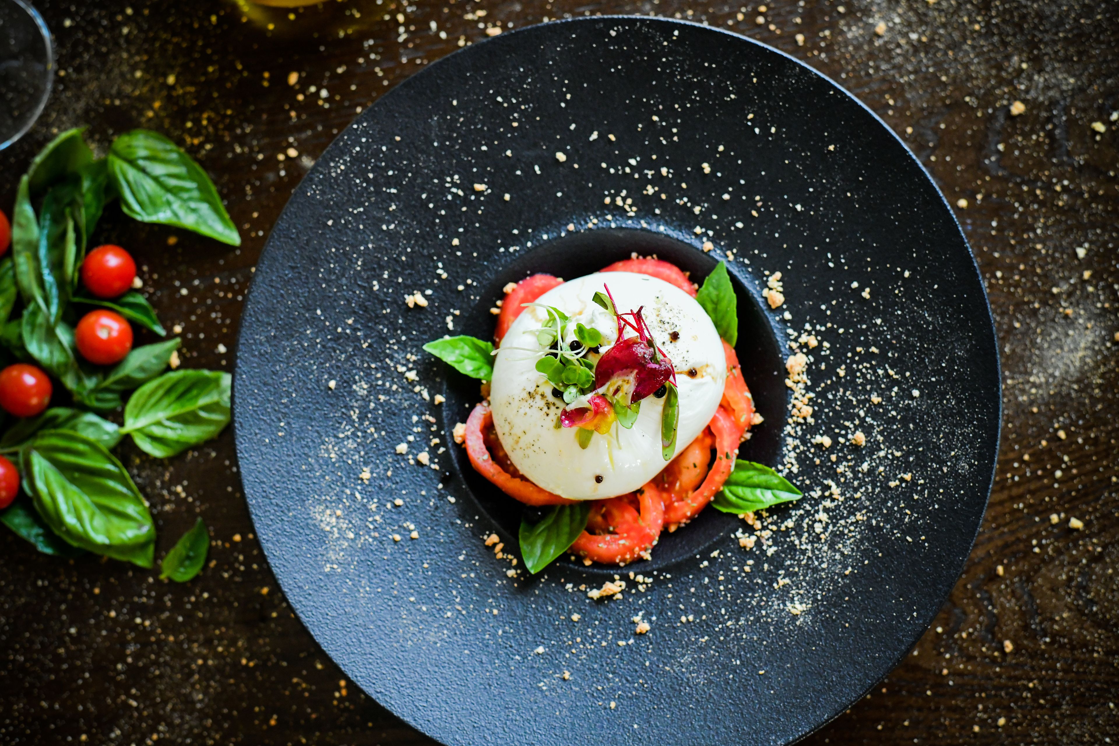 Een zwart bord met een schotel tomaten, mozzarella en basilicum.