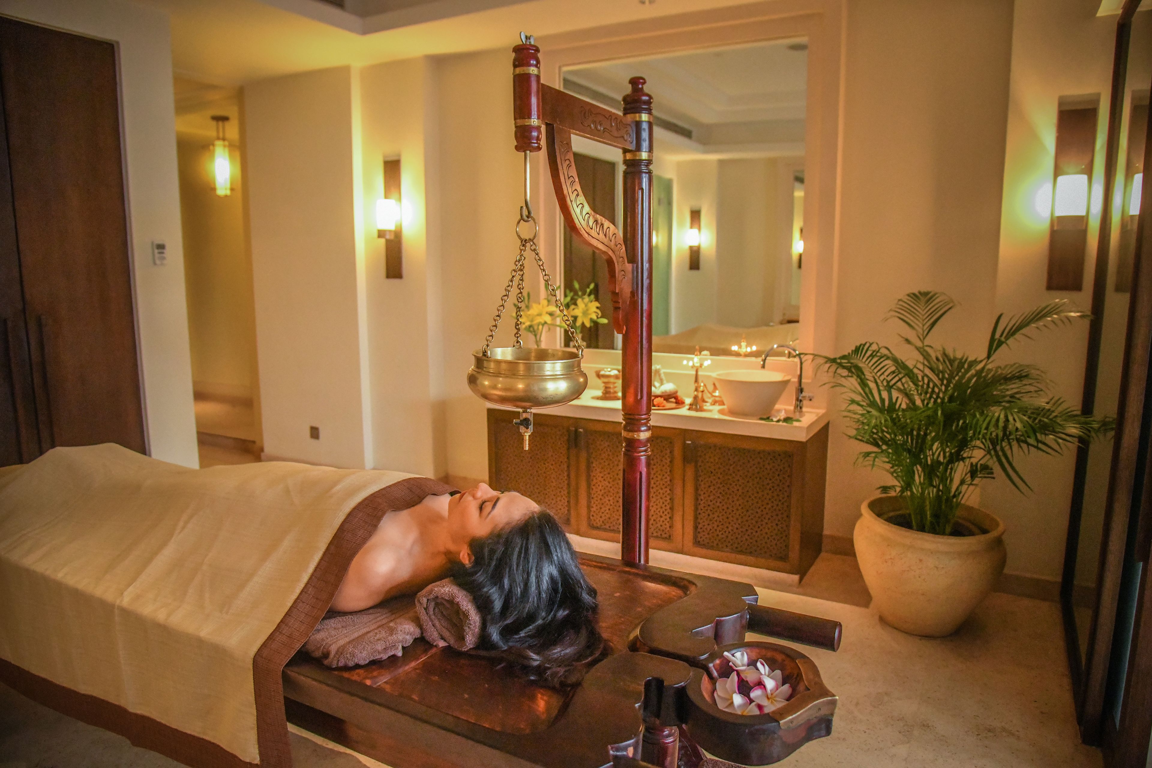 A spa room with a massage table, a wooden foot bath, a sink, and a potted plant.