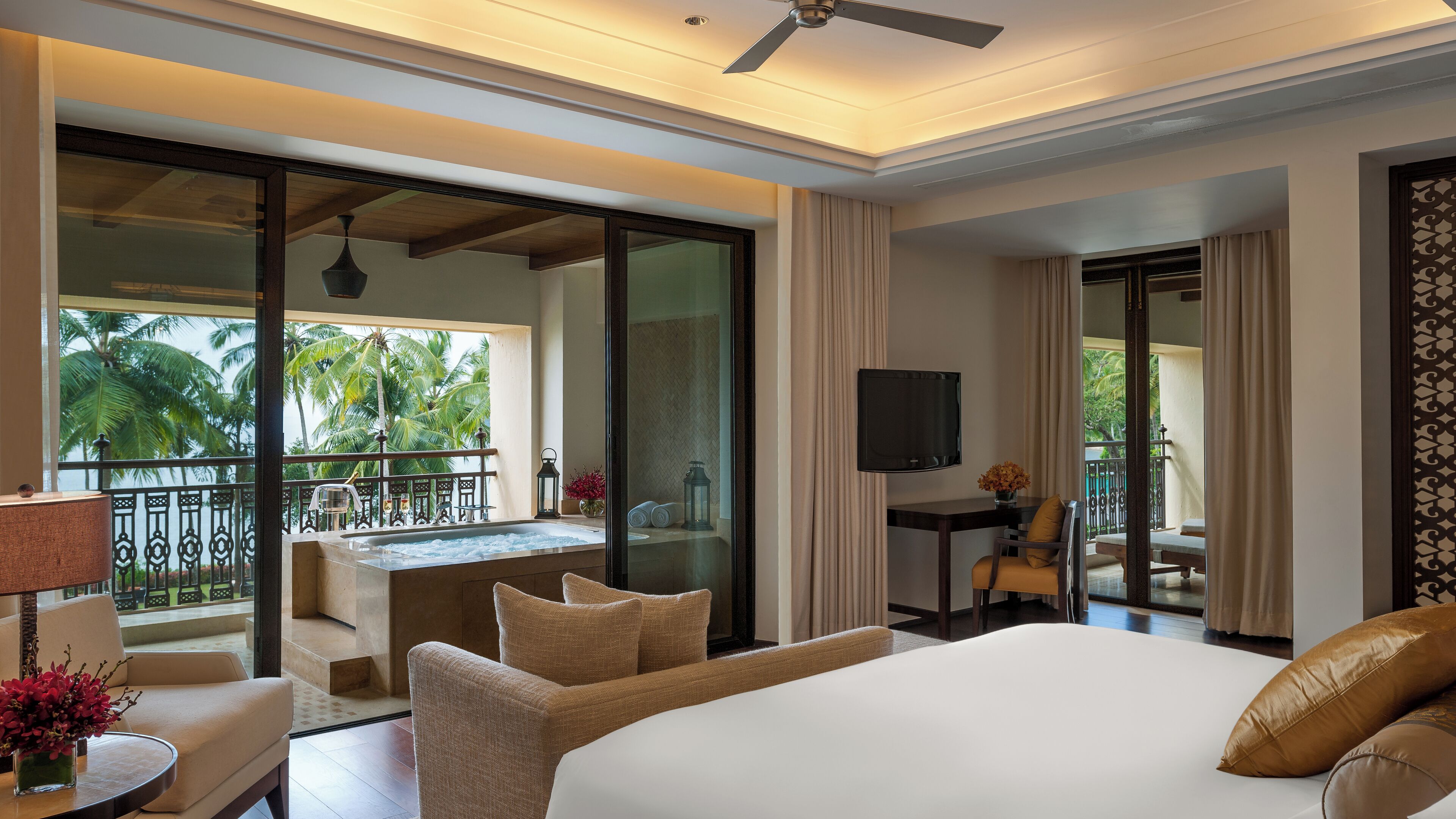 Una habitación de hotel con una cama grande, un escritorio con una silla, un televisor y un balcón con vistas a palmeras.