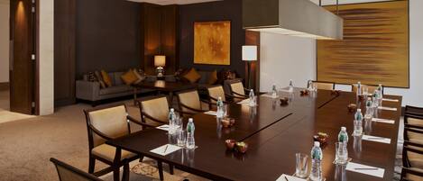 A conference room with a long table, chairs, water bottles, and a sofa in the background.