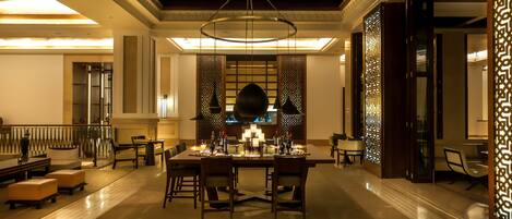 A spacious lobby with a central dining area, a chandelier, and a decorative wall with intricate patterns.