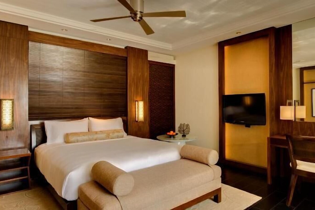 A hotel room with a large bed, a television, a desk, and a chair.