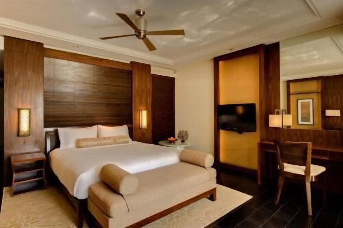 Habitación de hotel con una cama grande, un escritorio, una silla, un ventilador de techo y un televisor de pantalla plana.