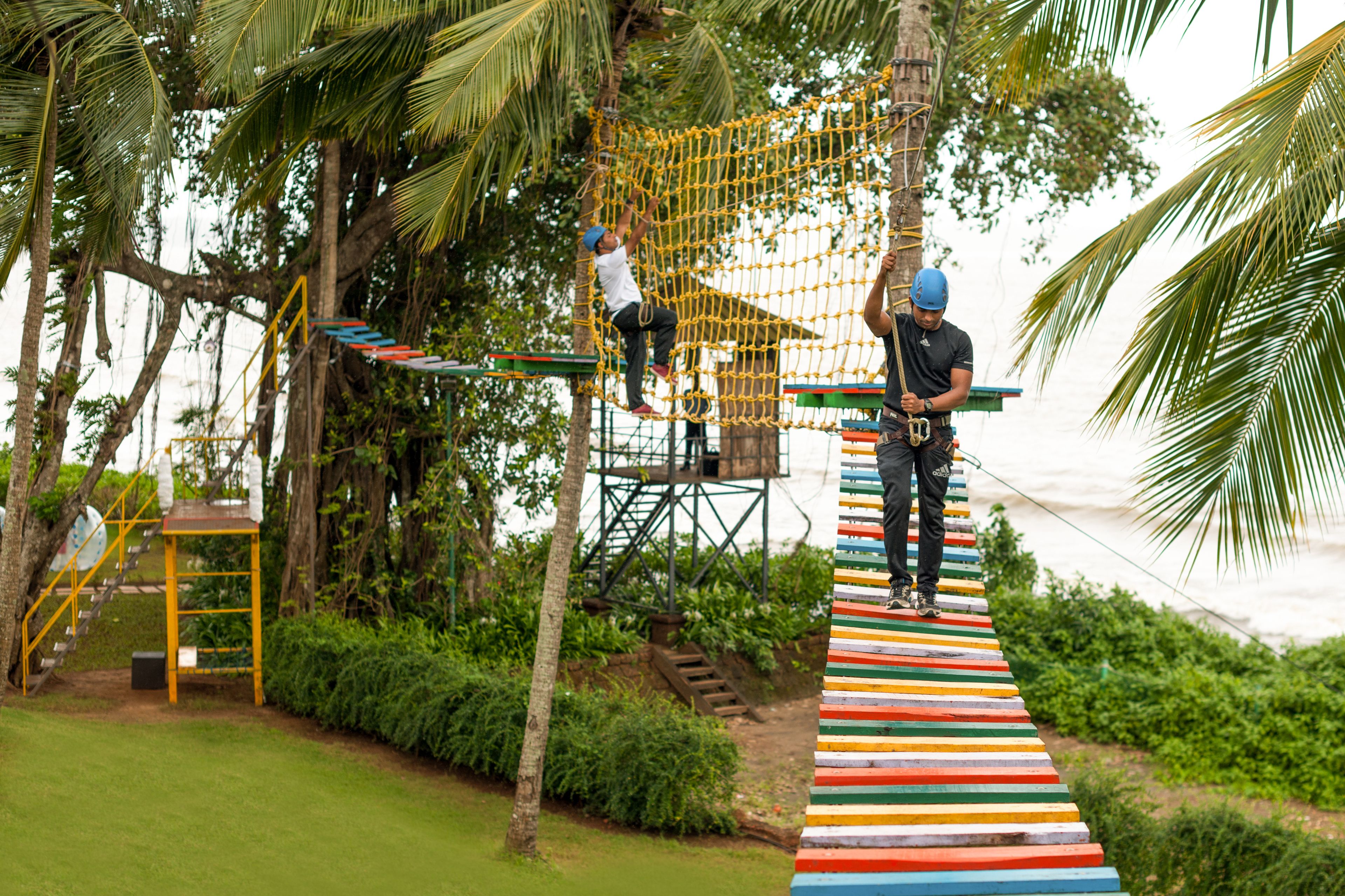 A rope bridge over a netted obstacle course in a tropical setting.