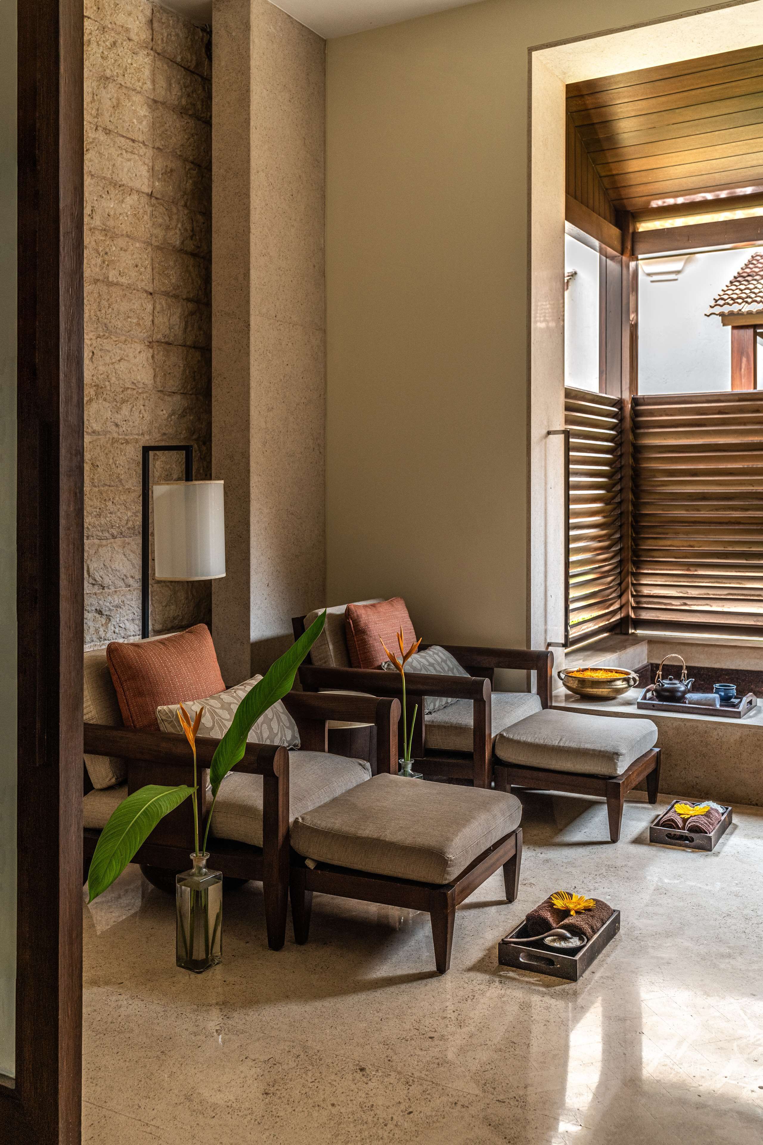 A cozy seating area with a stone wall, a lamp, and a window with wooden blinds.