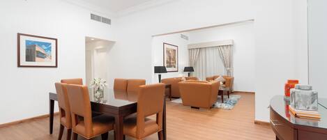 A modern living room with a dining area, featuring a wooden dining table, leather chairs, a sofa, and a coffee table.