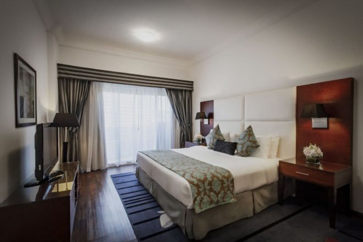 Habitación de hotel con una cama grande, mesitas de noche, un escritorio y una ventana con cortinas.