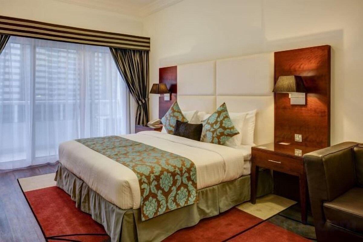 A hotel room with a large bed, a desk, a chair, and a view of the city.