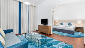 Una camera d'albergo con un letto, una poltrona, una televisione, un tavolino da caffè in vetro e un comodino con una lampada.