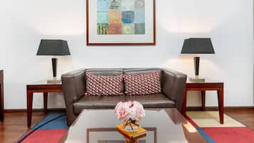 Una sala de estar con un sofá de cuero marrón, dos mesitas de noche con lámparas, una obra de arte abstracta enmarcada y un jarrón con flores sobre una mesa de centro.