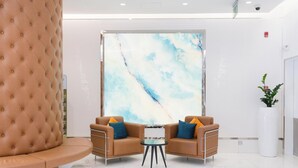 Un'ampia hall moderna con una panca in pelle traforata, due poltrone in pelle con cuscini blu e arancioni, un tavolino rotondo e un grande quadro astratto appeso alla parete.