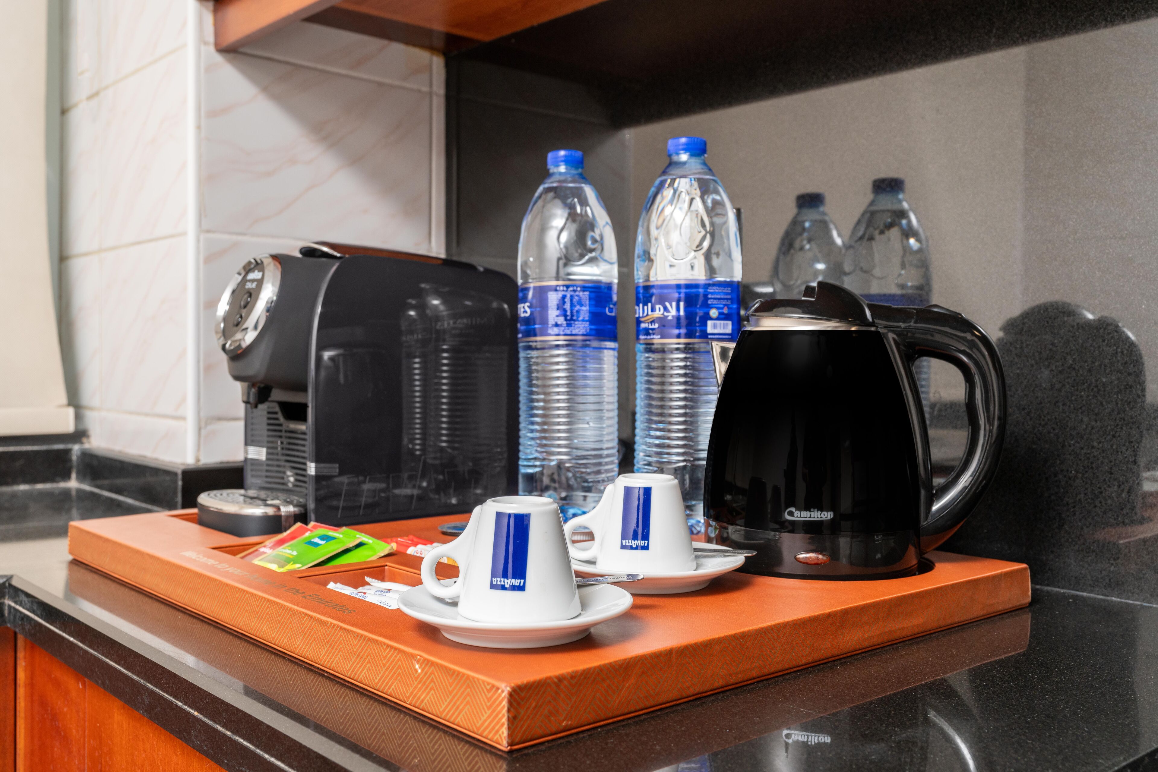 A hotel breakfast setup with a coffee maker, two cups, and water bottles on a tray.