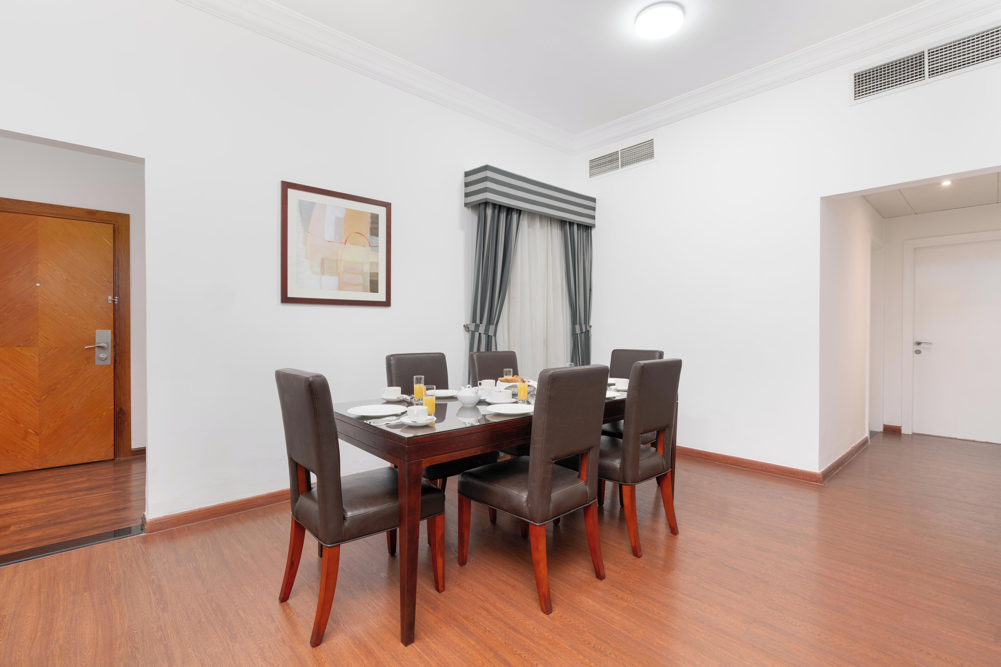 Un comedor con mesa y sillas de madera, un cuadro en la pared y una ventana con cortinas.