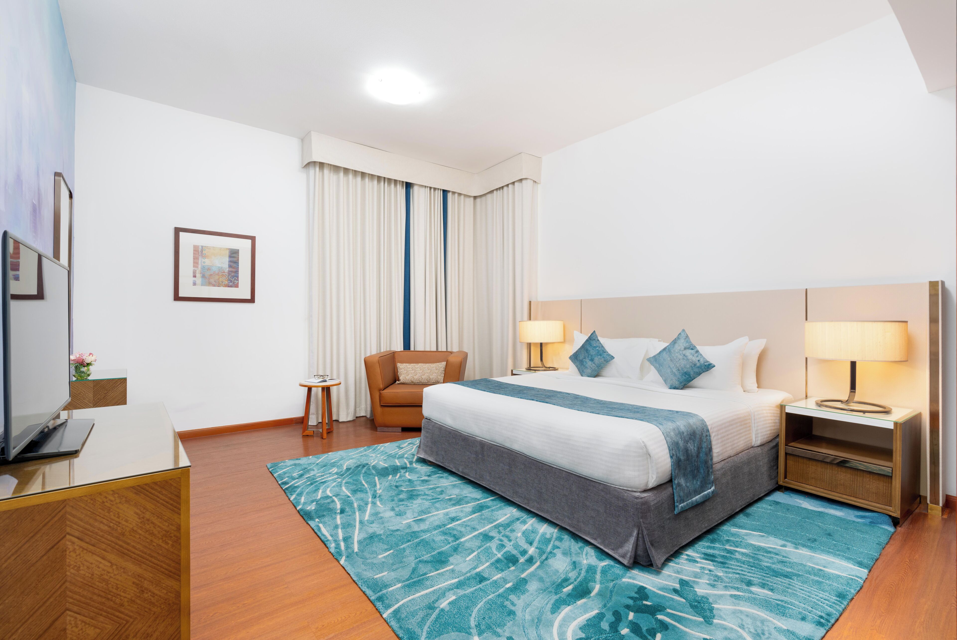 A modern hotel room with a large bed, a TV, a desk, and a chair.